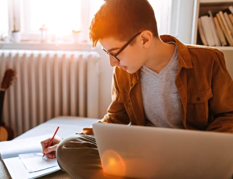 Student taking notes ate home with his laptop